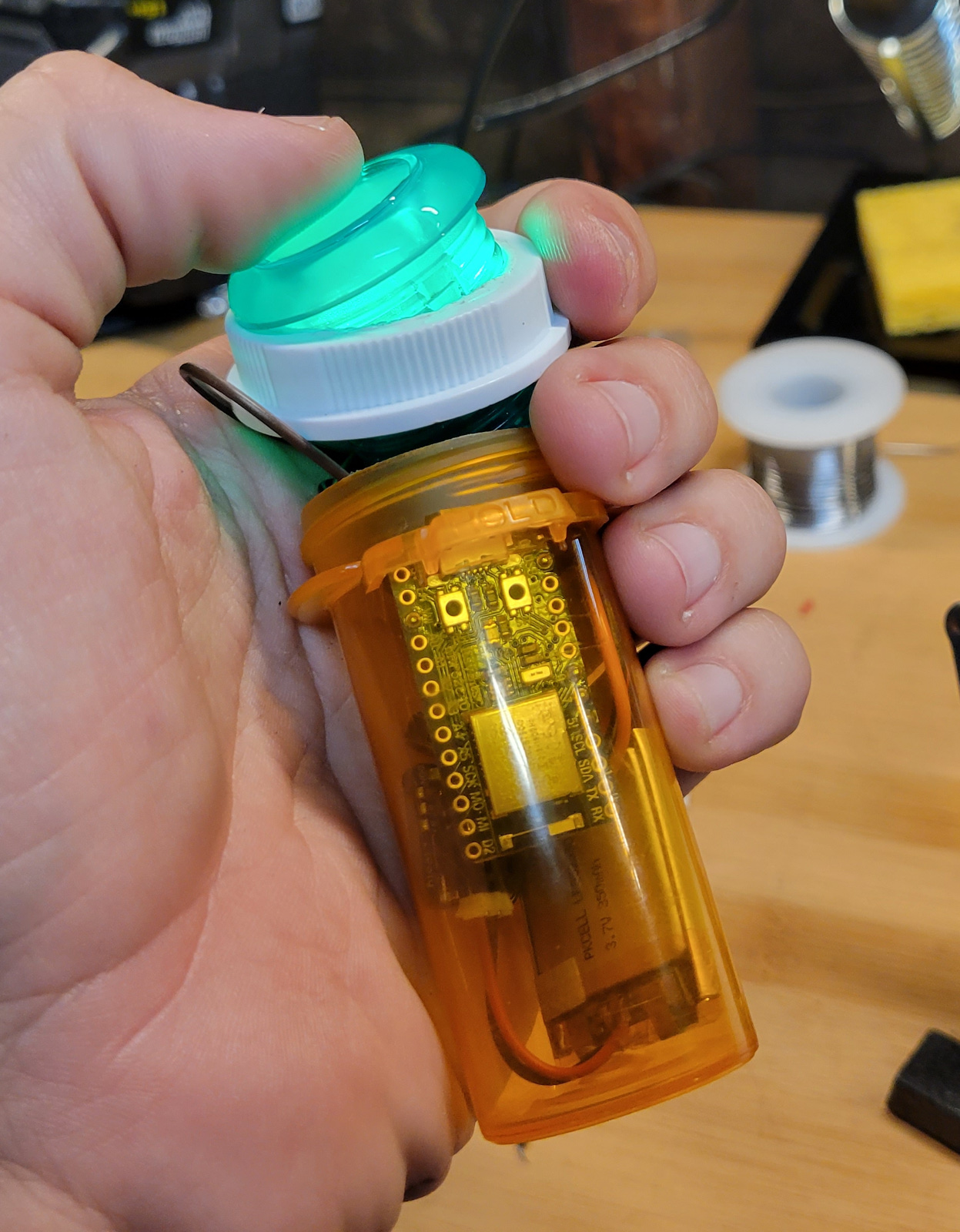 Sliding the circuit board and button through the top of hole in the lid and into the bottle.