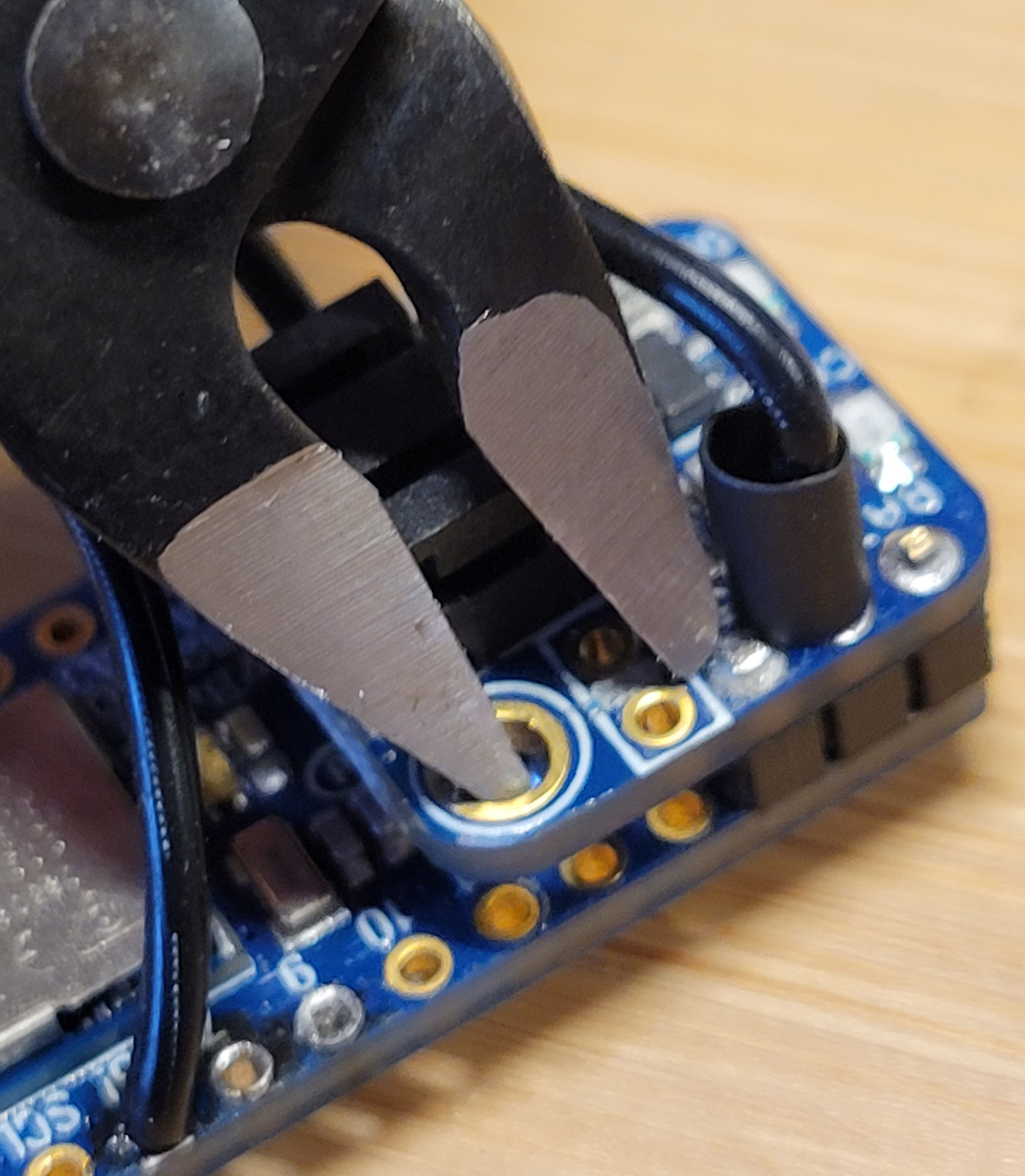 Using the flush cutter to cut the trace of the LiPo Backpack. One 'tooth' of the cutter is inside the mounting hole while the other drags across the trace to cut it.